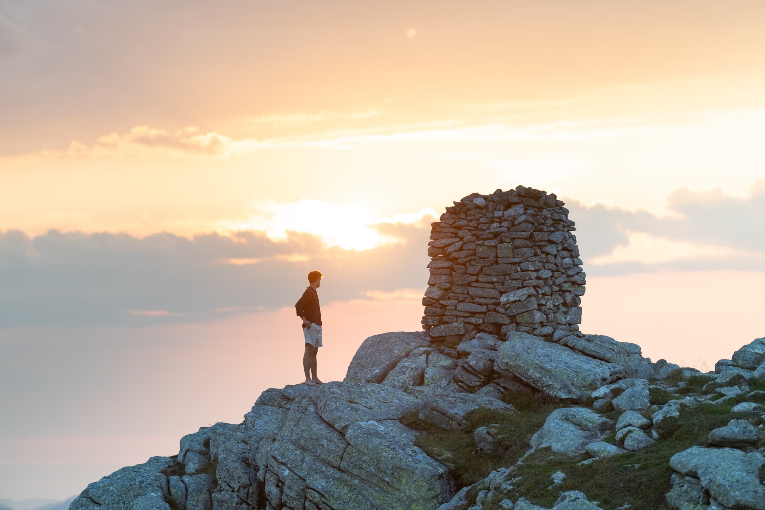 Utkikk fra fjelltopp med varde mot solnedgang